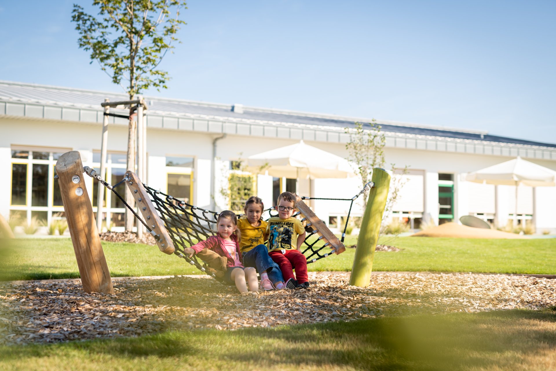 Kindergarten Drei Kinder sitzen in einer Hängematte auf dem Außengelände eines Kindergartens.