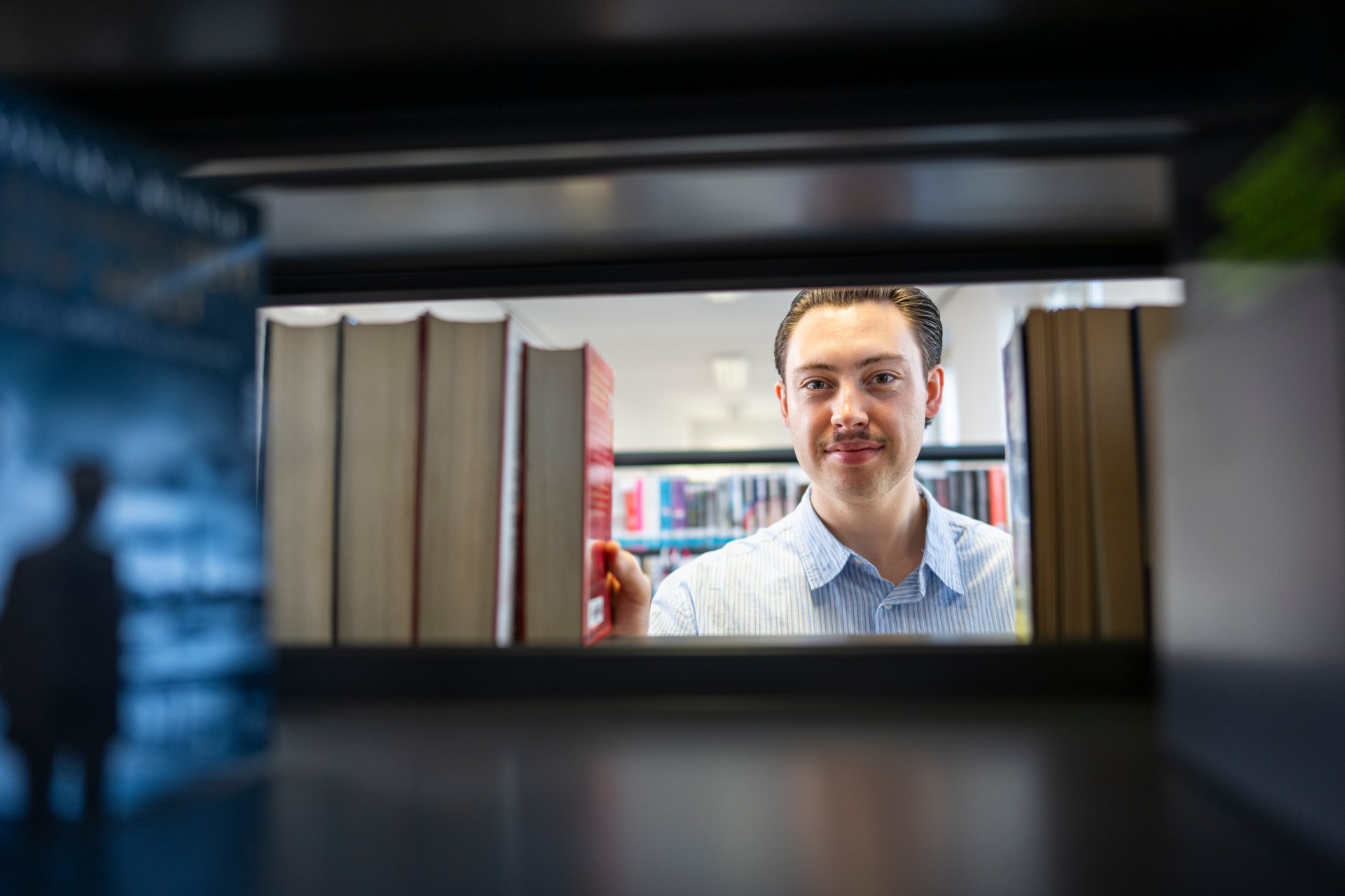City library Mann schaut zwischen Büchern durch.