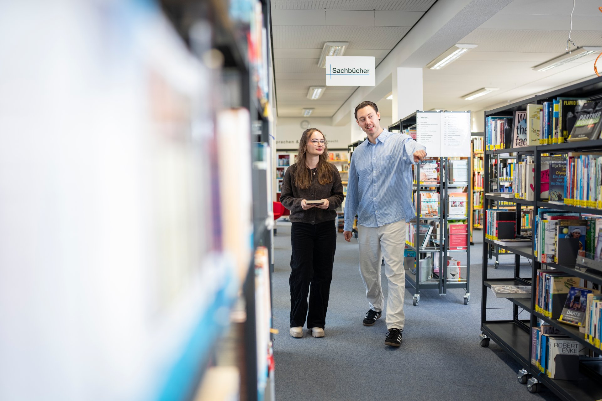 City library Ein Mann berät eine Frau in der Stadtbücherei zwischen den Regalen.