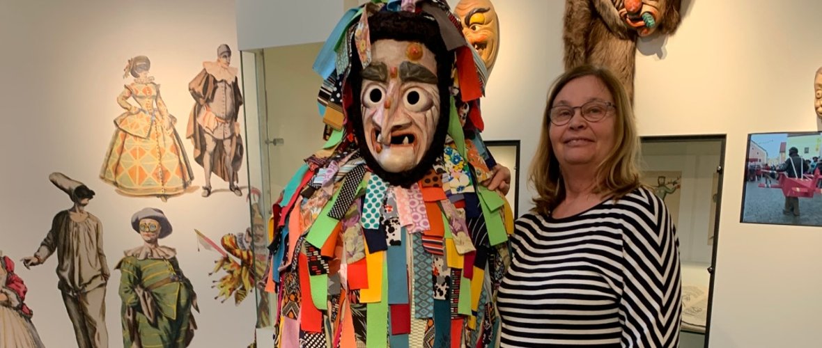A tour guide stands next to a colourful carnival figure