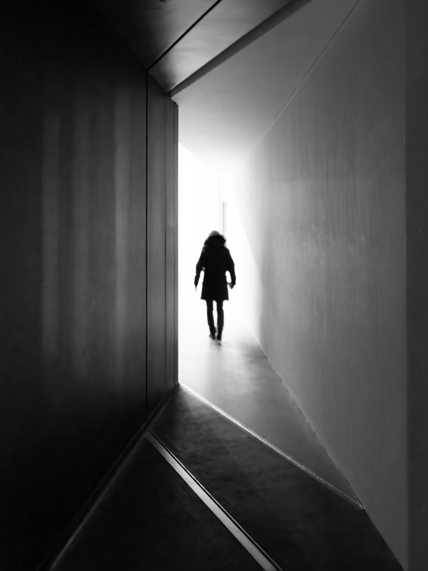 Eine Person läuft in einem Gebäude aus dem Schatten auf das Licht zu.