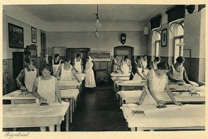 Bügelsaal in der Industrie- und Haushaltungsschule. Mehrere Frauen üben das richtige Bügeln unter Aufsicht und Anleitung.