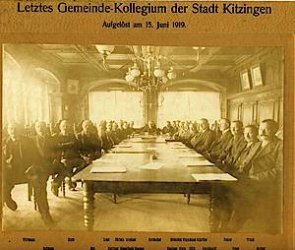 Letztes Gemeindekollegium von Michael Korbacher 1919. Alle Gemeinderatsmitglieder sitzen im Historischen Sitzungssaal an einer langen Tafel zusammen.